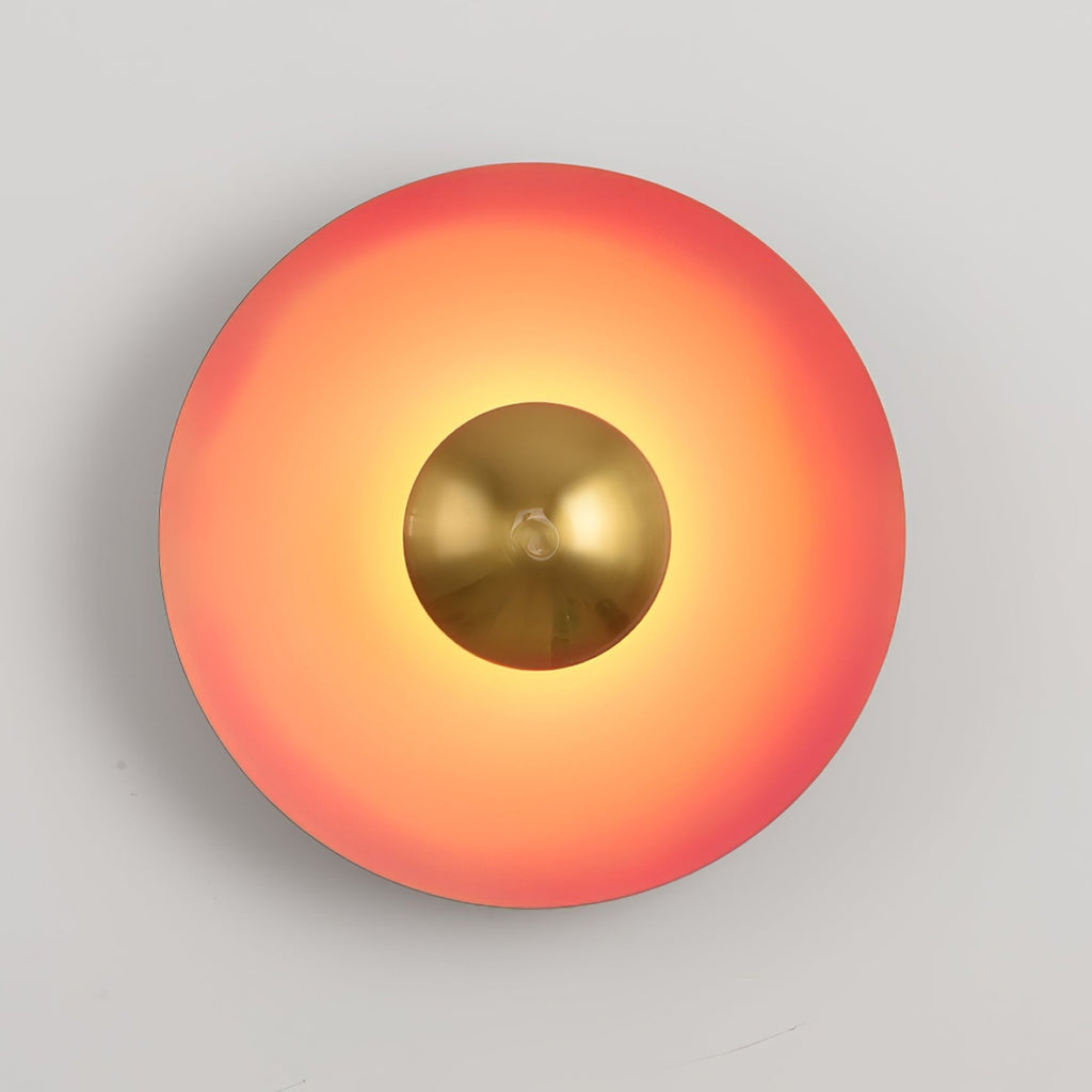 Warm light spreads from the antique copper centre of this coral-orange Clérachic wall light, on grey.