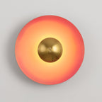 Warm light spreads from the antique copper centre of this coral-orange Clérachic wall light, on grey.