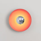 The mirrored centre of this coral-orange Clérachic wall light reflects the studio setting, shown on grey.