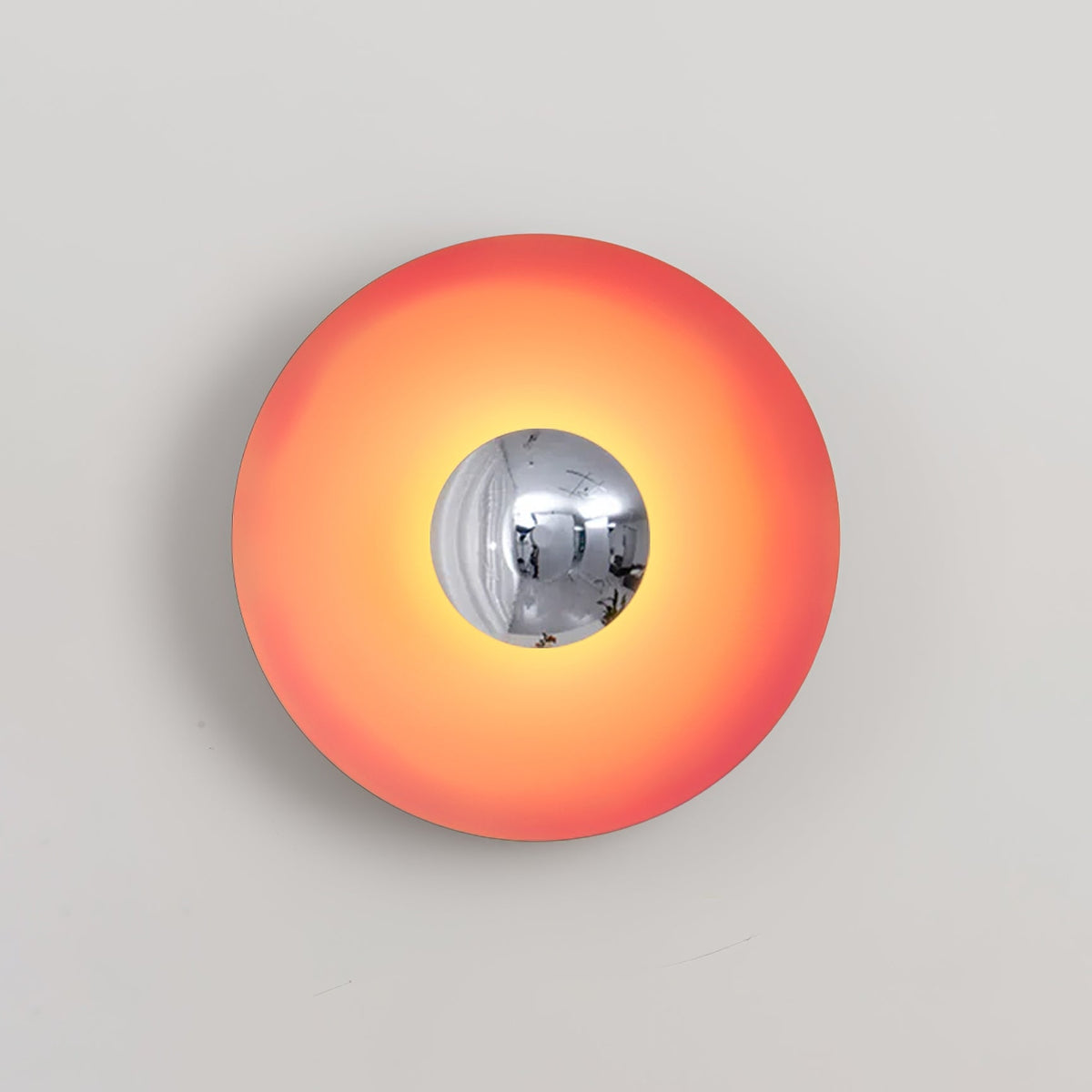 The mirrored centre of this coral-orange Clérachic wall light reflects the studio setting, shown on grey.