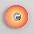 The chrome centre of this coral-orange Clérachic wall light reflects a soft highlight, shown on grey.