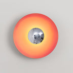 This coral-orange Clérachic wall light's chrome centre catches a warm highlight, isolated against grey.