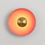 Seen straight-on, this coral-orange Clérachic wall light glows warm around its antique copper centre, on grey.
