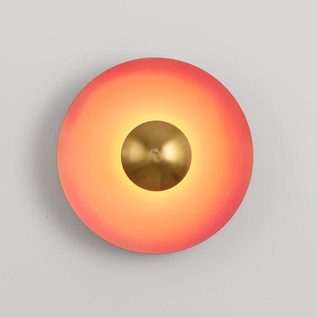 Seen straight-on, this coral-orange Clérachic wall light glows warm around its antique copper centre, on grey.