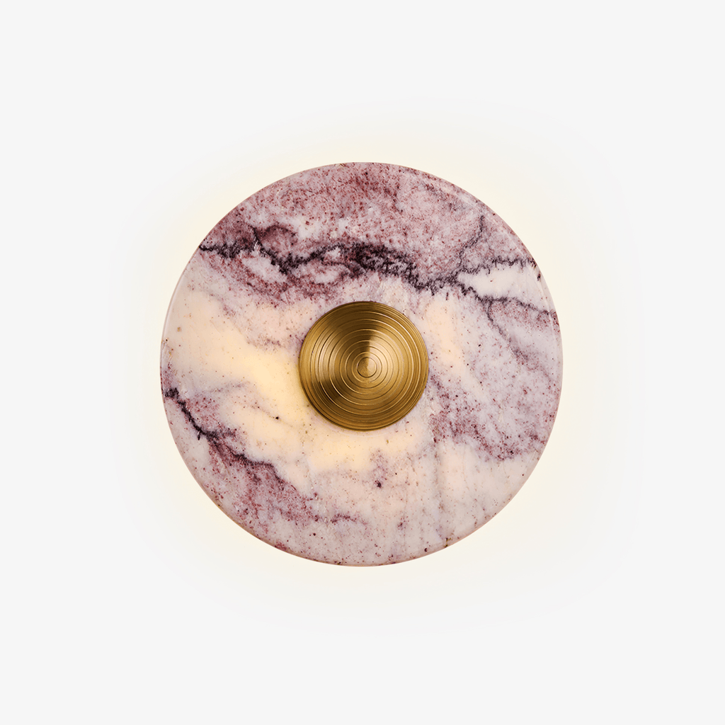 A purple marble disc wall light from Clérachic on a plain background, its gold ridged centre knob framed by a warm backlit halo.