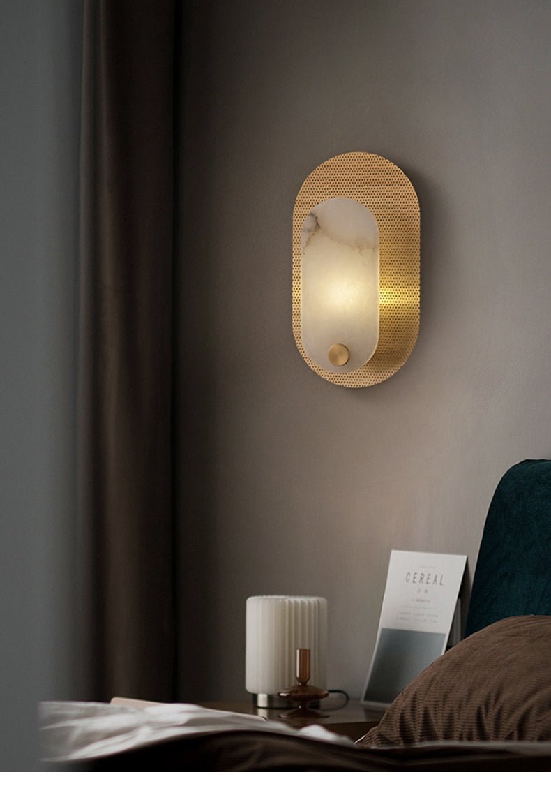 The lit sconce above a nightstand, a ribbed candle holder and magazine below it.