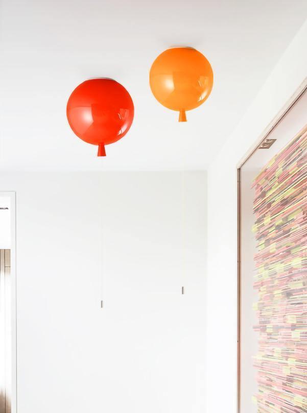 Two Clérachic balloon lights in red and orange hang from a white ceiling-wall corner near a patterned door.