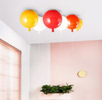 Against a pink wall with wood blinds, four Clérachic balloon lights in yellow, red, white and orange hang above a planter box.