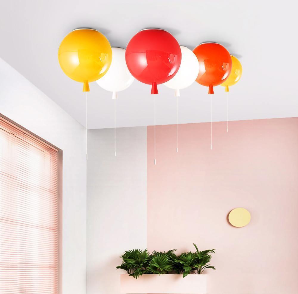 Against a pink wall with wood blinds, four Clérachic balloon lights in yellow, red, white and orange hang above a planter box.