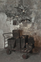 Black bird-shaped pendants from this Clérachic fixture hang above a cart of terracotta pots against a weathered wall.