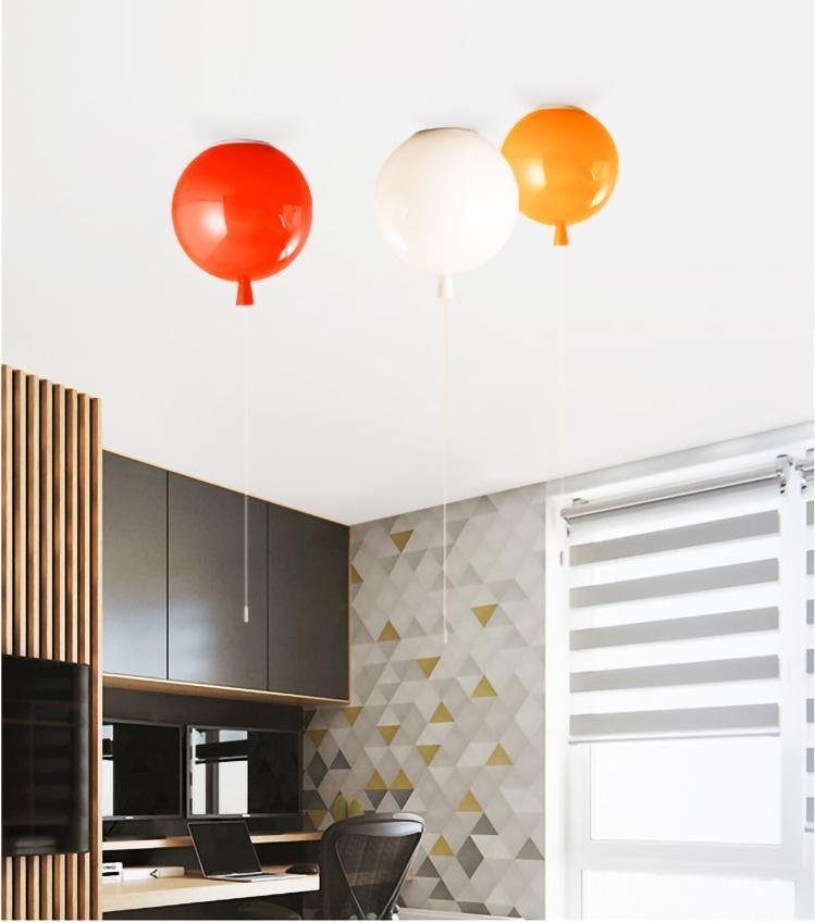Above a desk with triangle-patterned wallpaper, three Clérachic balloon lights in red, white and orange hang near a roller blind.