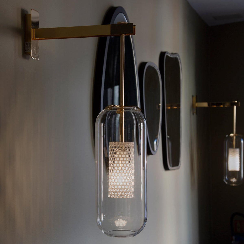 Glass wall lamp with slim arm glowing in a styled interior