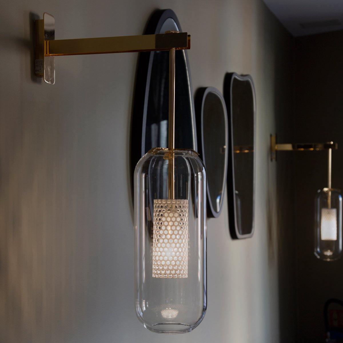 Glass wall lamp with slim arm glowing in a styled interior