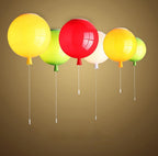Six Clérachic balloon lights in yellow, green, red and orange float together against a warm golden-brown backdrop.
