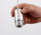 A hand holds the nickel LED driver cylinder of this Clérachic pendant, unattached, on a plain white backdrop.
