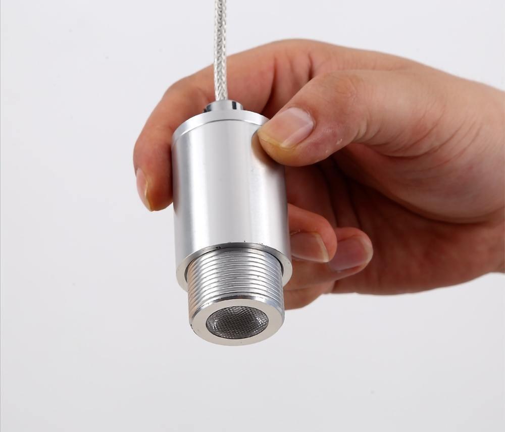 A hand holds the nickel LED driver cylinder of this Clérachic pendant, unattached, on a plain white backdrop.