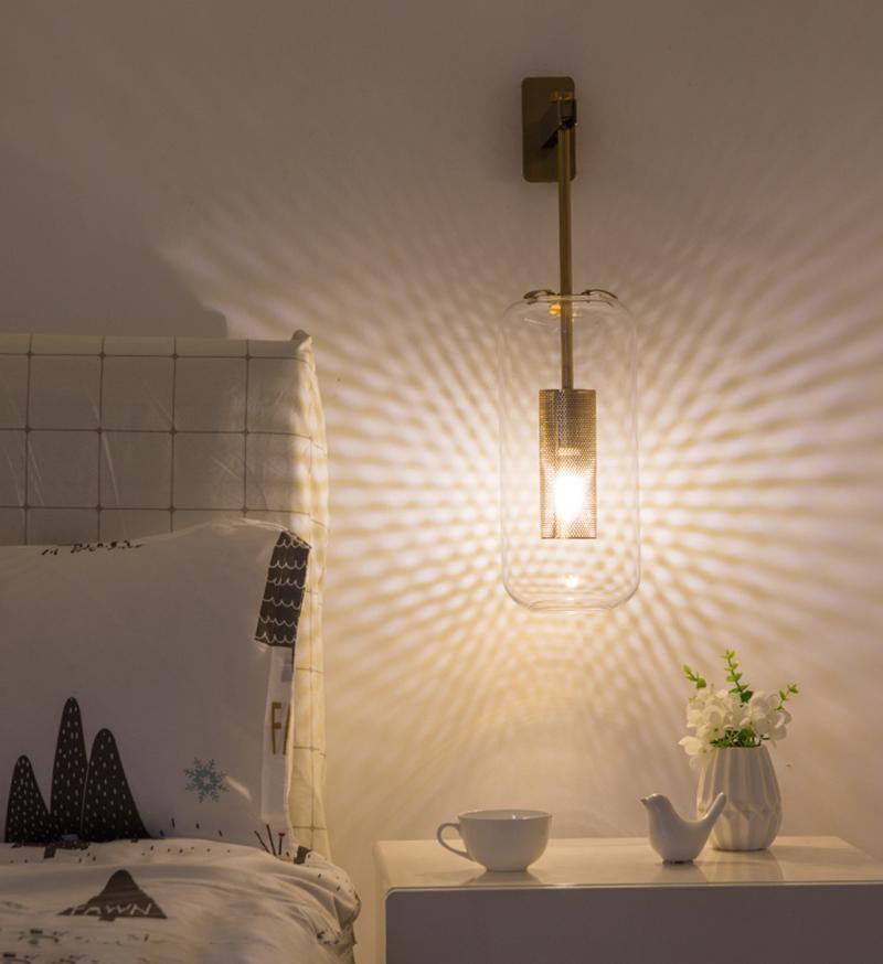 Glass wall lamp with metal arm glowing beside a bedside table