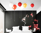 Six Clérachic balloon lights in white, red and yellow tones hang above a bed with a black mural wall behind.