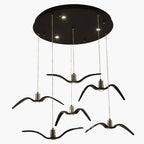Six black bird-shaped pendants from this Clérachic fixture hang from a round black canopy, seen from above.