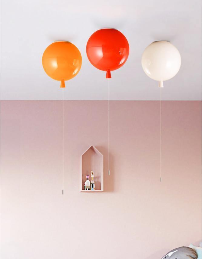 Against a soft pink wall, three Clérachic balloon lights in orange, red and white hang beside a small wooden house shelf.