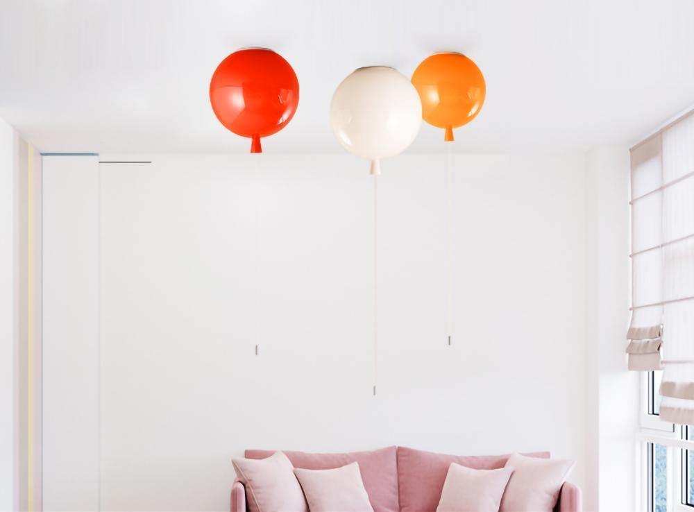 Above a blush-pink sofa, three Clérachic balloon lights in red, white and orange hang from a white ceiling corner.