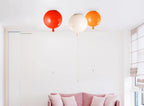 Above a blush-pink sofa, three Clérachic balloon lights in red, white and orange hang from a white ceiling corner.