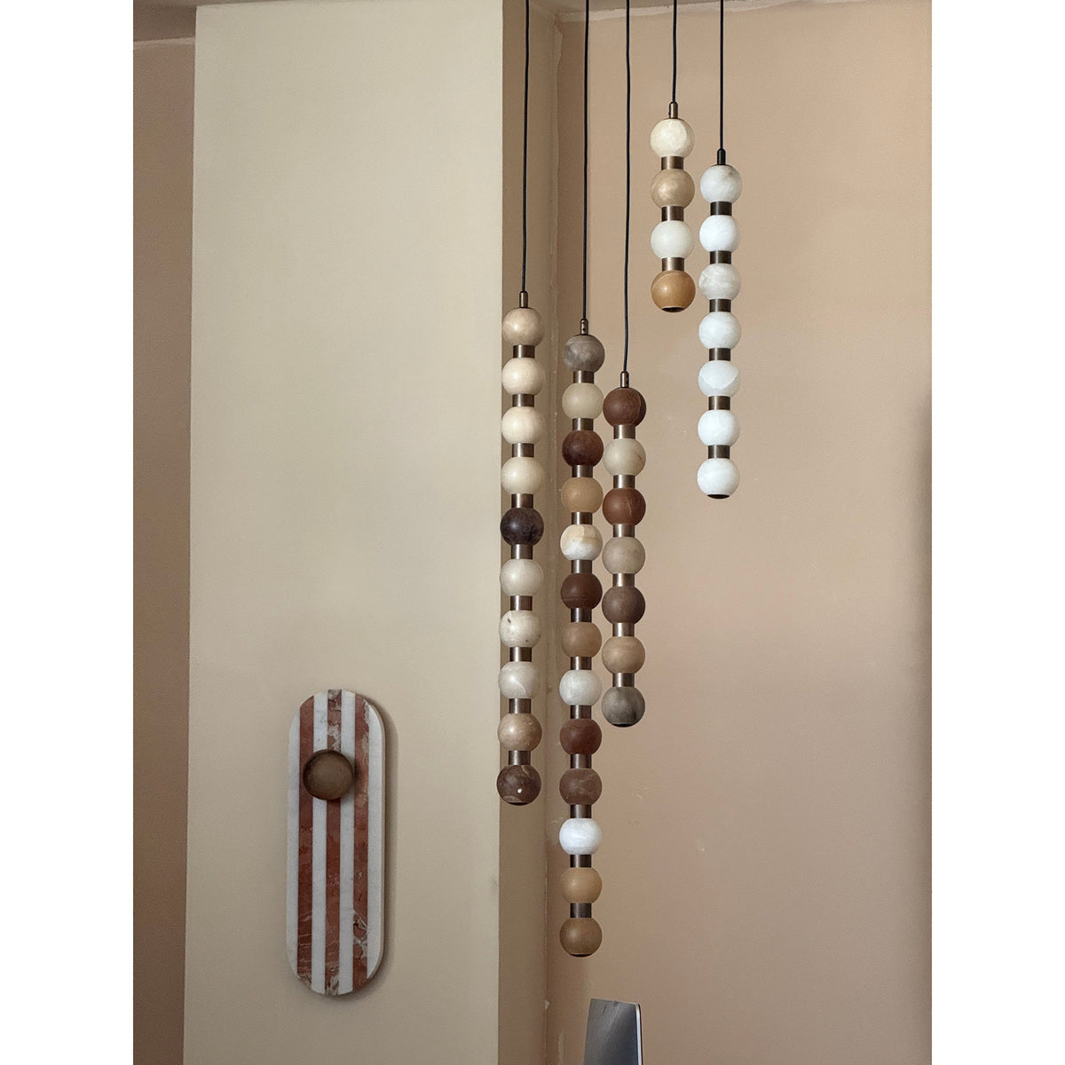 Several Clérachic alabaster sphere pendants of different lengths hang together near a striped wall sconce.