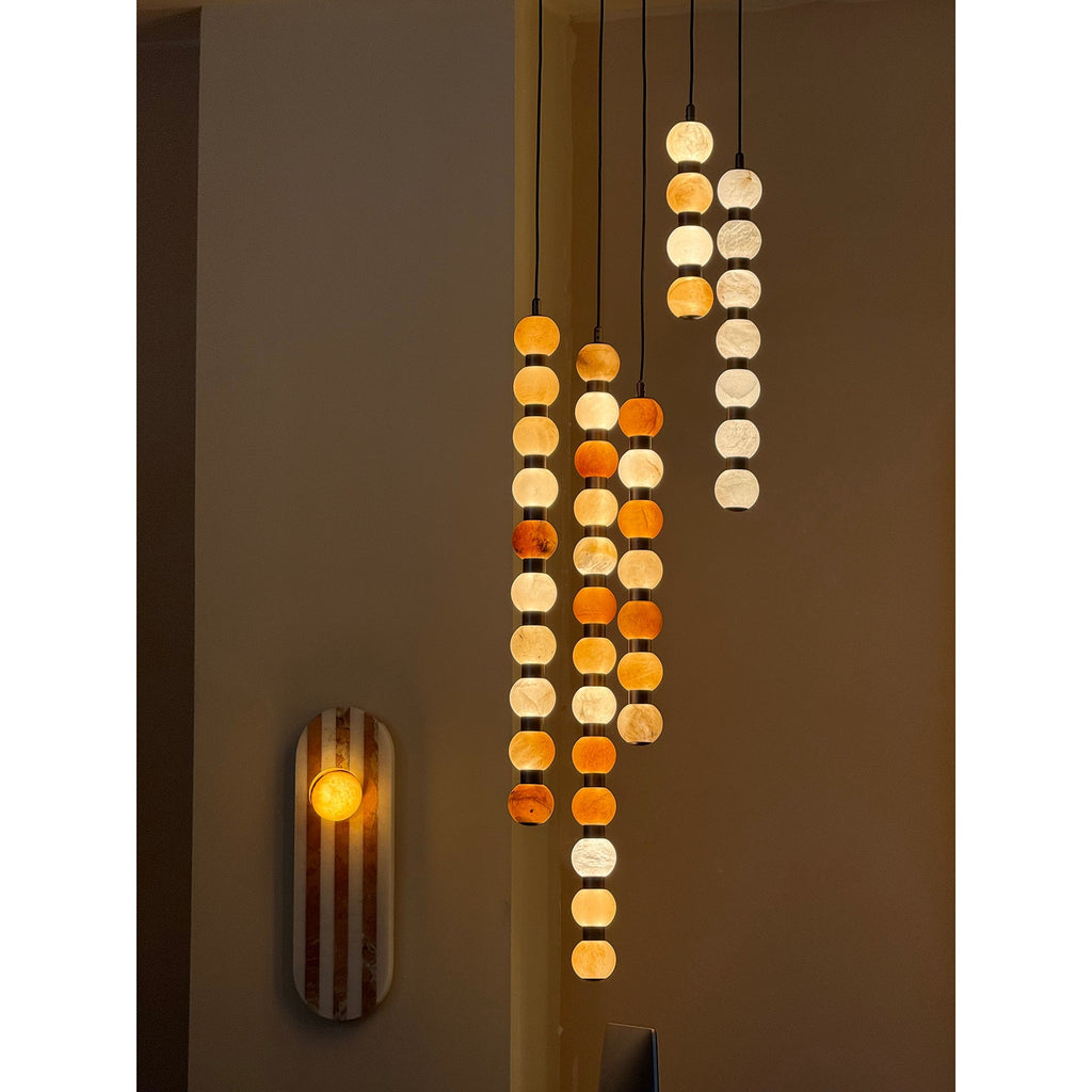 Three Clérachic alabaster sphere pendants hang together near a striped wall sconce in a dim room.