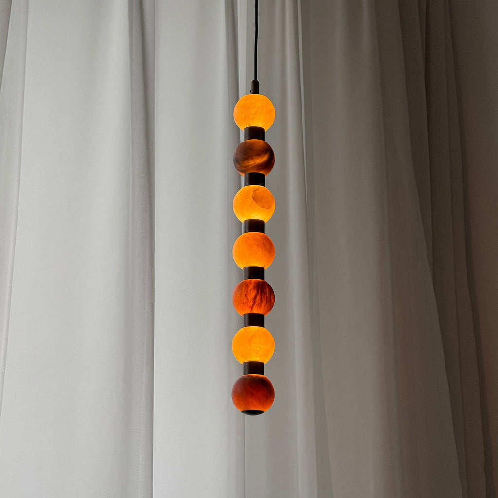 Close view of the alabaster spheres on this Clérachic pendant, their veining warmly lit against a sheer curtain.