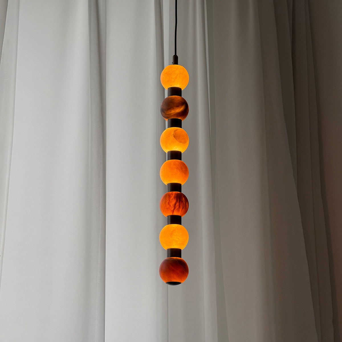 Close view of the alabaster spheres on this Clérachic pendant, their veining warmly lit against a sheer curtain.