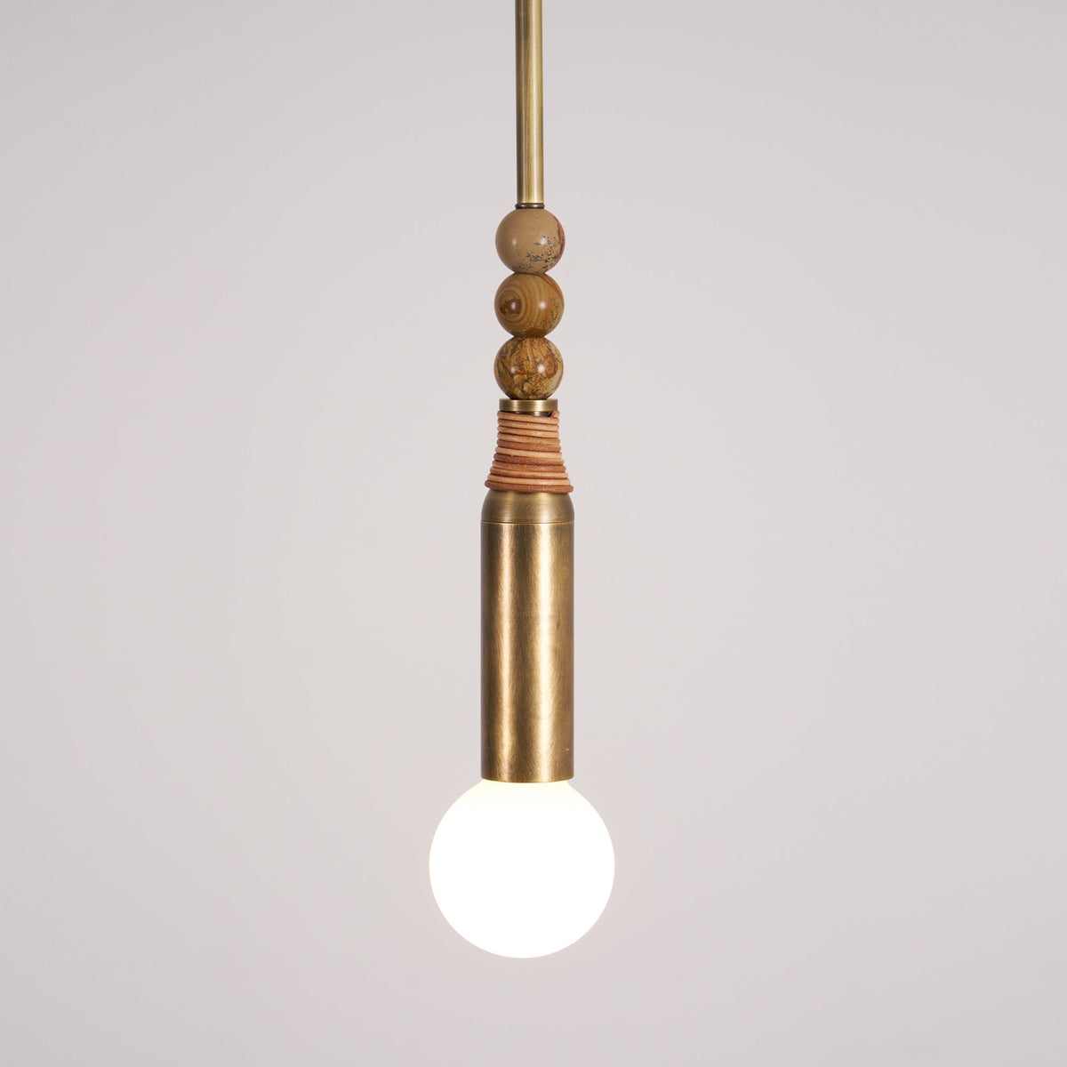 Detail shot of the Clérachic pendant's marble beads and leather wrap, with the bare bulb glowing beneath them.