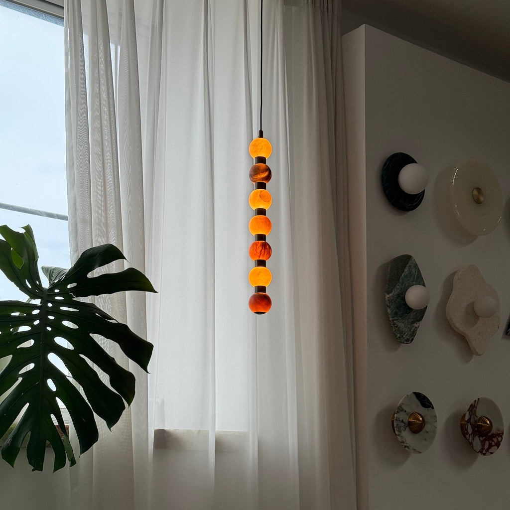 A closer view catches the upper spheres of this Clérachic pendant glowing warm beside a wall of small round discs.