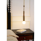 The Clérachic pendant light glows over a nightstand book, with the bed's cream linen pillow just visible in frame.