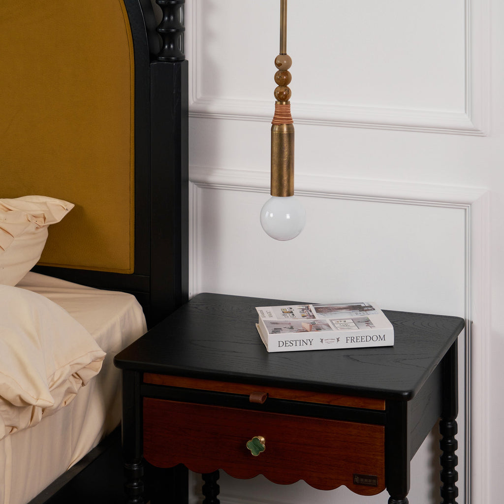 Close bedroom crop of the Clérachic pendant light above a nightstand drawer with a green pull and a magazine on top.