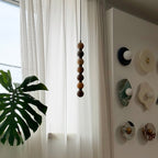 This Clérachic pendant's stacked alabaster spheres deepen from brown to bright orange, hanging beside a curtain and small wall discs.