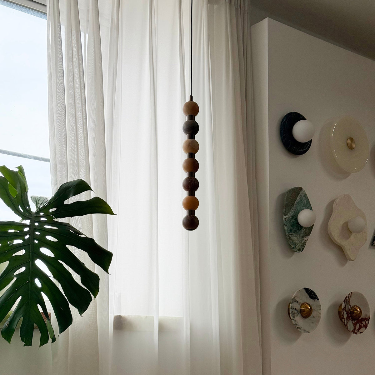 This Clérachic pendant's stacked alabaster spheres deepen from brown to bright orange, hanging beside a curtain and small wall discs.