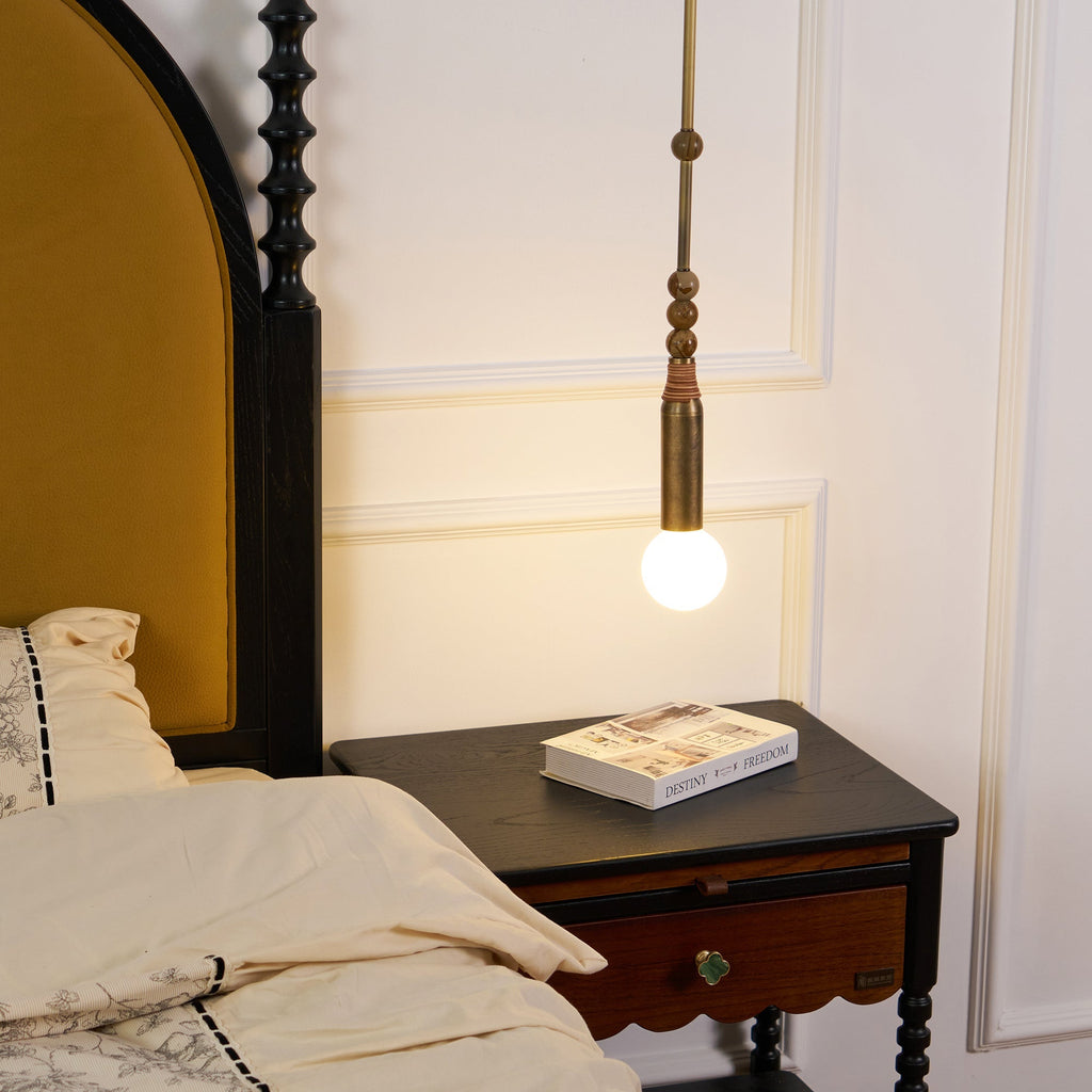A Clérachic marble-bead pendant light glows beside a four-poster bed, hanging just above a dark wood nightstand holding a book.