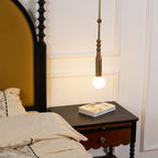 A Clérachic marble-bead pendant light glows beside a four-poster bed, hanging just above a dark wood nightstand holding a book.