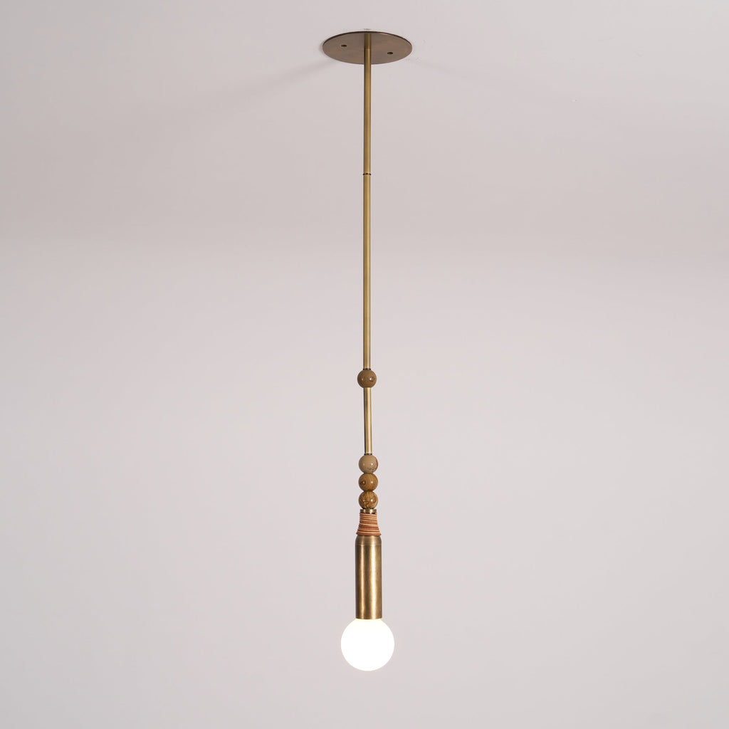 An antique brass Clérachic pendant light shown full length from its round ceiling canopy to the frosted bulb, on a plain backdrop.