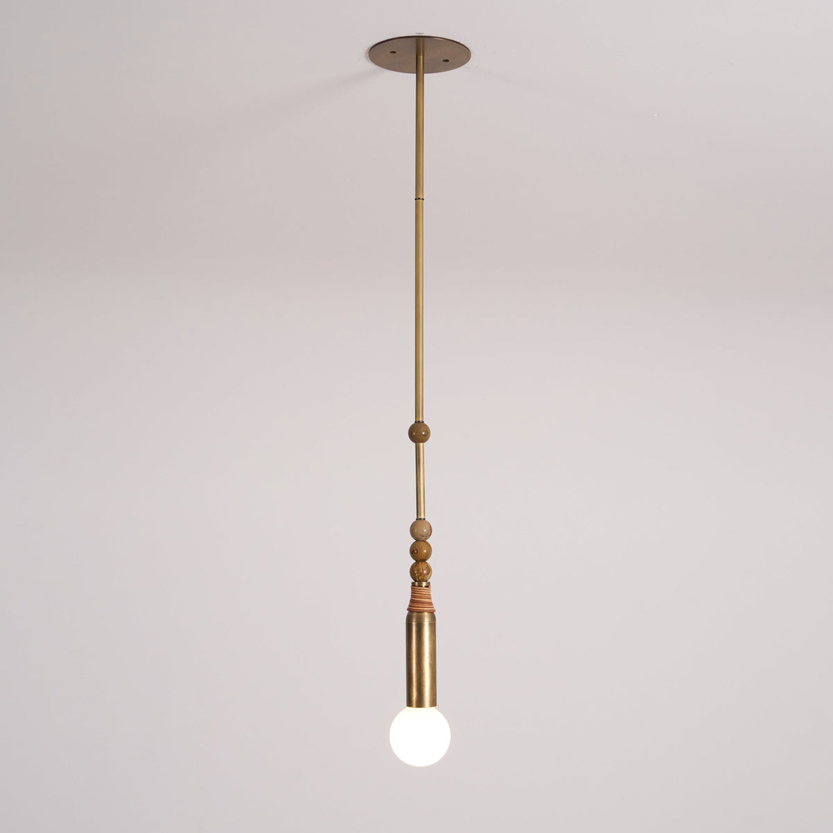 An antique brass Clérachic pendant light shown full length from its round ceiling canopy to the frosted bulb, on a plain backdrop.