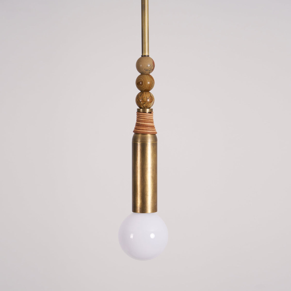 A closer view of the Clérachic pendant's marble bead stack and brass socket, with the frosted bulb glowing below.