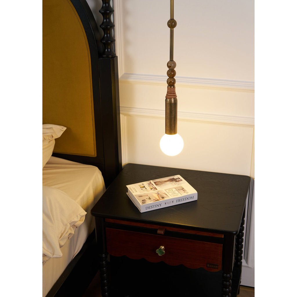 Wide bedroom shot of the Clérachic pendant light beside cream pillows and a dark wood nightstand with a closed drawer.