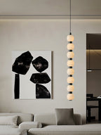 Tall view of the eight-ball Orbique pendant lit beside abstract art in a pale living room