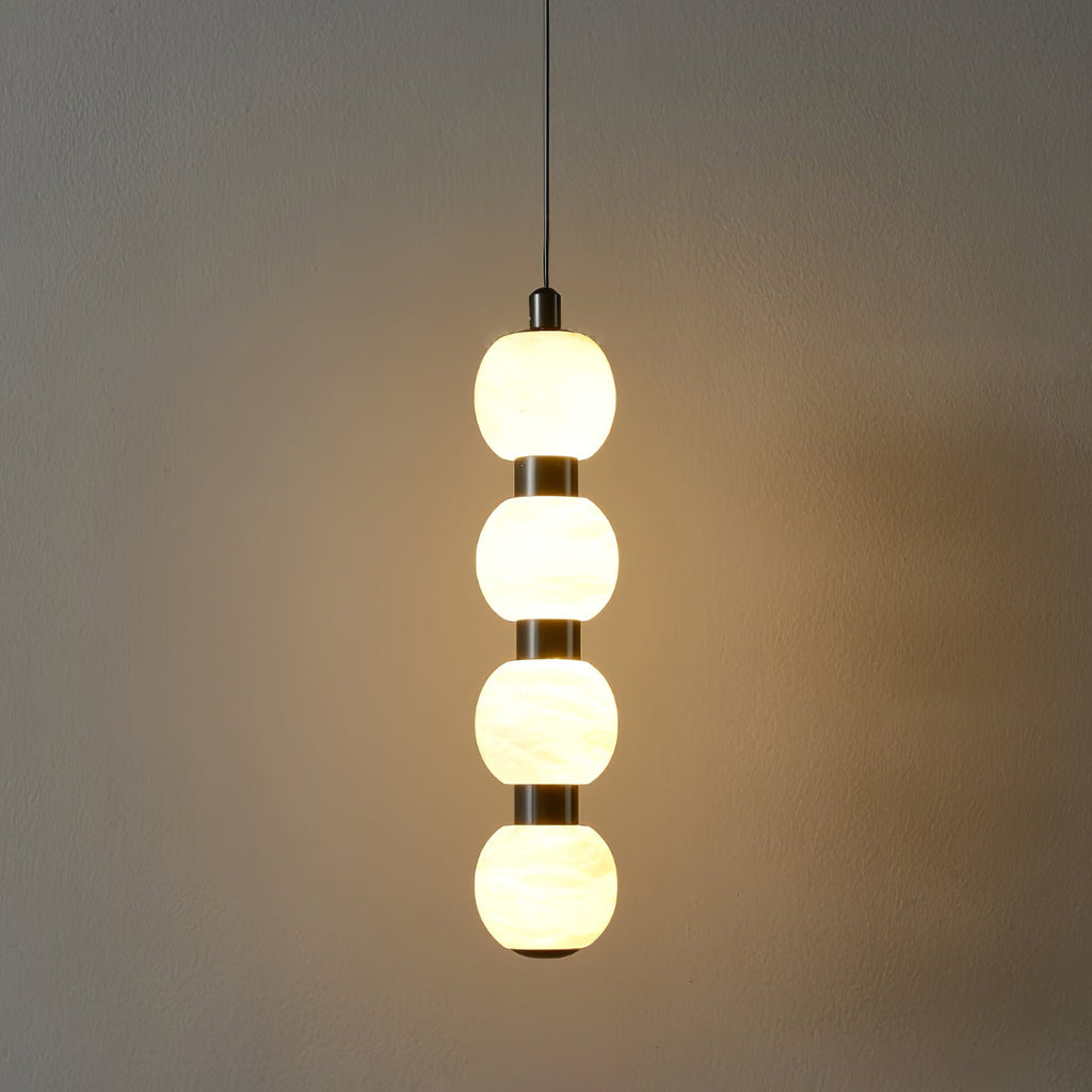 Four-ball Orbique pendant lit in a dark room, throwing a warm pool of light across the wall
