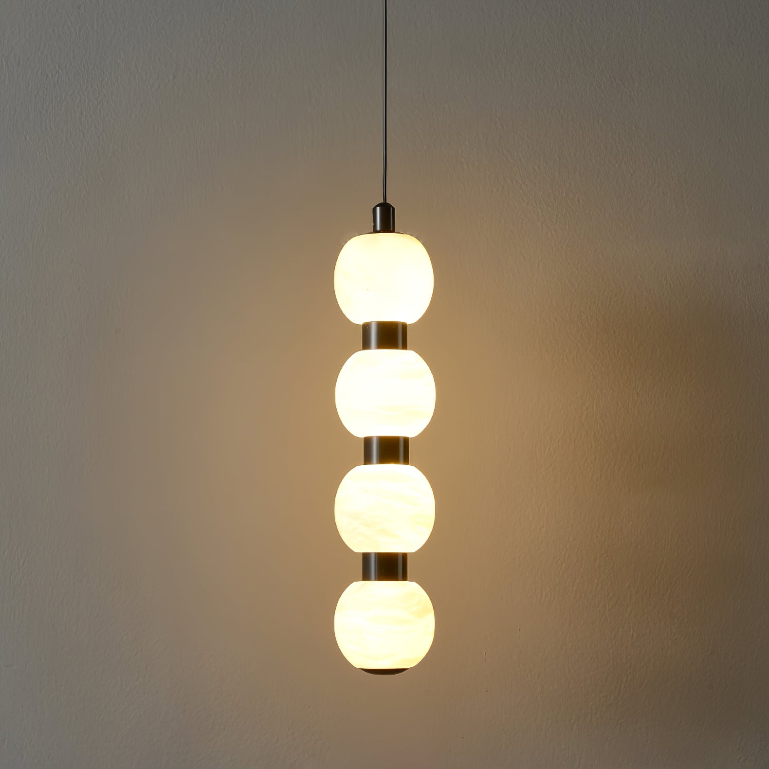 Four-ball Orbique pendant lit in a dark room, throwing a warm pool of light across the wall