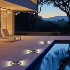 Three domed deck lights lit across poolside paving at dusk, with hills beyond the terrace.
