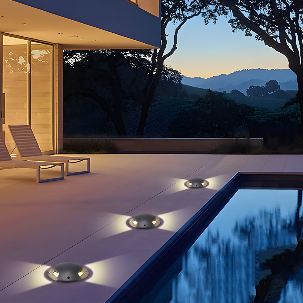 Three domed deck lights lit across poolside paving at dusk, with hills beyond the terrace.