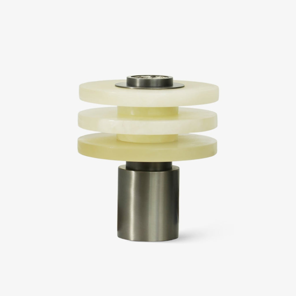 Tiered alabaster table lamp unlit on a plain white background, three stacked stone discs on a gunmetal base