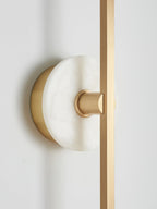 Close-up of a Clérachic wall sconce's pale alabaster disc where it meets the brass bar against a plain wall.