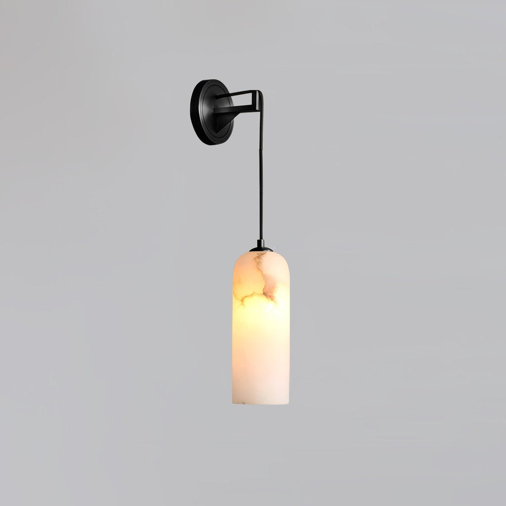 Vaelara alabaster wall sconce in the black finish, lit, with the cord dropping to the stone shade